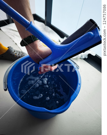 Window cleaner squeezing water from squeegee into bucket Window cleaner squeezing water from squeegee into bucket 124757086