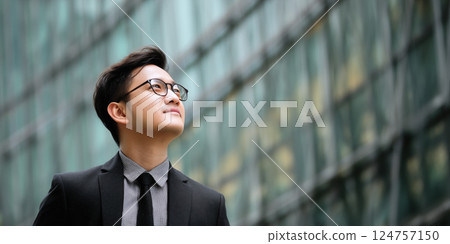 confident young businessman formal attire gazes upward with optimism against modern glass confident young businessman formal attire gazes upward with optimism against modern glass 124757150