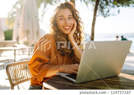 Young woman works at laptop on cafe terrace. Freelancer enjoying weather outdoors. Vacation concept. 124757287