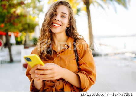 Portrait of a young woman holding a phone in her hands on a city avenue, on a sunny day. Portrait of a young woman holding a phone in her hands on a city avenue, on a sunny day. 124757291