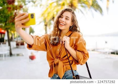 Tourist takes selfie with smartphone camera while walking along sunny streets of resort town. 124757292