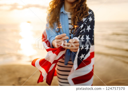 Young woman with American flag and sparklers on beach. Patriotic holiday. USA celebrate 4th of July. 124757370