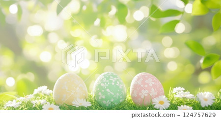 Three colorful Easter eggs with delicate floral patterns resting on fresh green grass, surrounded by tiny white daisies. Sunlight filters through vibrant leaves, creating a dreamy bokeh background 124757629