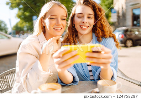 Two smiling woman are sitting in a cafe, drinking coffee. Fashion, beauty, blogging, tourism. Two smiling woman are sitting in a cafe, drinking coffee. Fashion, beauty, blogging, tourism. 124758287