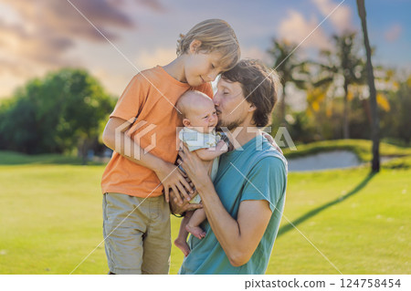 Father, older son, and newborn baby on a meadow in the park. Family spending quality time together in nature. Parenthood, love, and family bond concept Father, older son, and newborn baby on a meadow in the park. Family spending quality time together in nature. Parenthood, love, and family bond concept 124758454