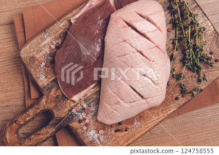 Fresh raw duck breasts, on a wooden chopping board, with herbs and spices, no people 124758555