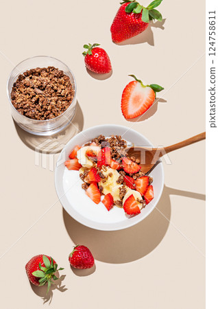 Greek yogurt with chocolate granola, strawberries and banana in a bowl on a beige background 124758611