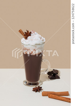 Hot chocolate with whipped cream, cinnamon and spices in a tall glass on a beige background 124758622
