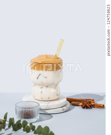 Korean whipped drink Dalgona coffee in a glass on a marble stand on a blue background with cinnamon. Korean whipped drink Dalgona coffee in a glass on a marble stand on a blue background with cinnamon. 124758623