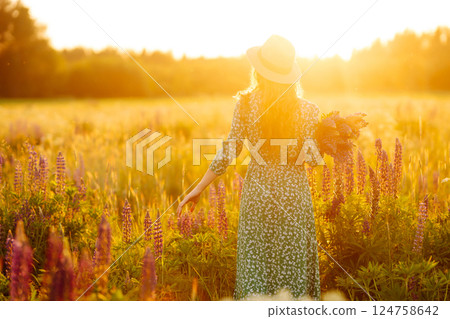 Stylish woman in a straw hat with a bouquet of flowers on a field with lupins. Lifestyle concept. Stylish woman in a straw hat with a bouquet of flowers on a field with lupins. Lifestyle concept. 124758642
