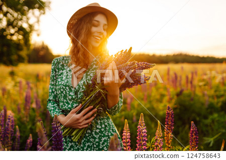 Stylish woman in a straw hat with a bouquet of flowers on a field with lupins. Lifestyle concept. Stylish woman in a straw hat with a bouquet of flowers on a field with lupins. Lifestyle concept. 124758643