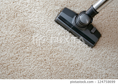 Overhead close-up of a black vacuum cleaner head moving across a fluffy beige carpet 124758699