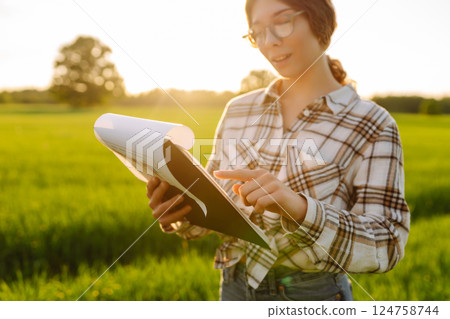 Young female farmer is studying with tablet young wheat in the field. Concept for farm development. Young female farmer is studying with tablet young wheat in the field. Concept for farm development. 124758744
