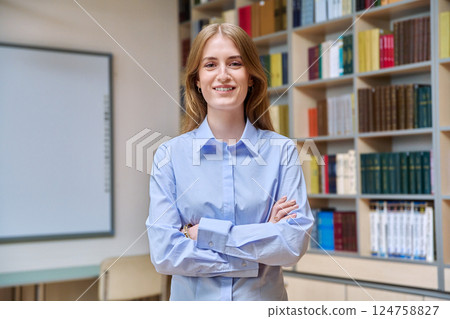 Portrait of teenage college student girl with crossed arms, inside library 124758827