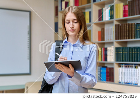 Portrait of student teenager girl using digital tablet inside classroom library Portrait of student teenager girl using digital tablet inside classroom library 124758829