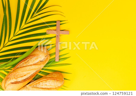 A wooden cross with a Bible and bread on a palm leaves pattern, a Palm Sunday theme A wooden cross with a Bible and bread on a palm leaves pattern, a Palm Sunday theme 124759121