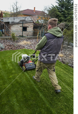 Nitra, Slovakia - 04.02.2025: A man trims the grass with a trimmer on the lawn. Mowing the lawn. Nitra, Slovakia - 04.02.2025: A man trims the grass with a trimmer on the lawn. Mowing the lawn. 124759552