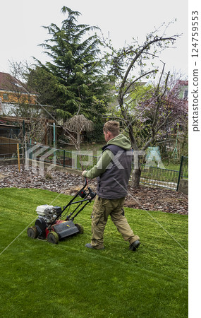 Nitra, Slovakia - 04.02.2025: Man trims the grass with a trimmer on the lawn. Mowing the lawn. 124759553
