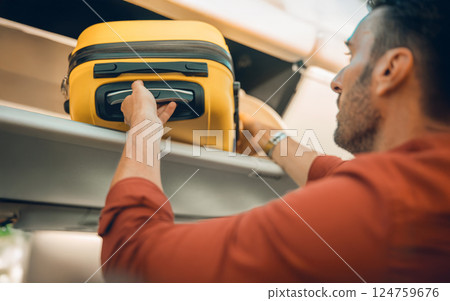 A man is currently placing his yellow suitcase into the overhead cabin on an airplane A man is currently placing his yellow suitcase into the overhead cabin on an airplane 124759676