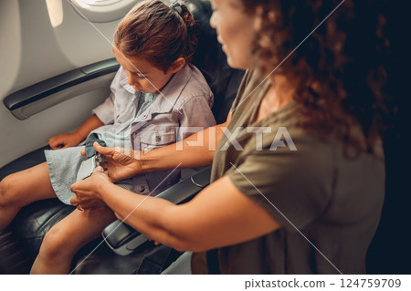 A Parent Helps Their Child to Securely Fasten the Seatbelt While on an Airplane, Ensuring Safety 124759709
