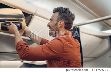 A Passenger Carefully Placing Their Luggage in the Overhead Compartment on an Airplane 124759727