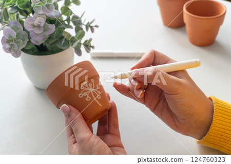 Decorating a small terracotta clay flower pot with a white marker Decorating a small terracotta clay flower pot with a white marker 124760323