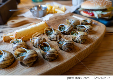 Delicious escargot and sliced bread on wooden board with burger in background Delicious escargot and sliced bread on wooden board with burger in background 124760326
