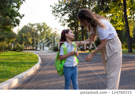 Mother guiding daughter to school on a sunny morning walk Mother guiding daughter to school on a sunny morning walk 124760355