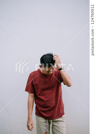 Contemplative man scratching head against a minimalist wall backdrop Contemplative man scratching head against a minimalist wall backdrop 124760912