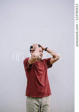 Man holding his head in distress against a plain background Man holding his head in distress against a plain background 124760913