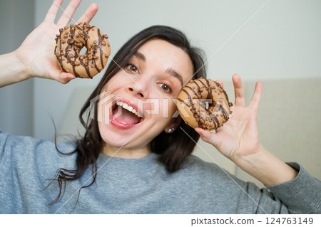 Funny smiling girl posing with a couple of glazed cappuccino donuts Funny smiling girl posing with a couple of glazed cappuccino donuts 124763149