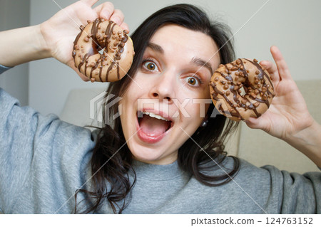 Funny smiling girl playing with a couple of glazed cappuccino donuts 124763152