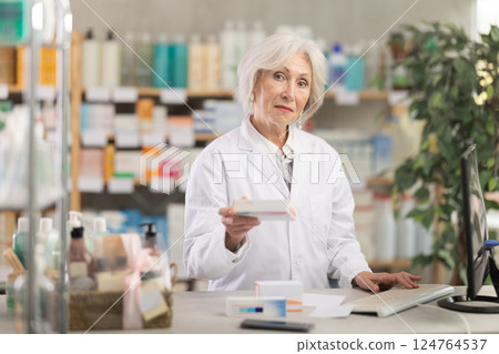 Mature female pharmacist offering a box of medicines 124764537
