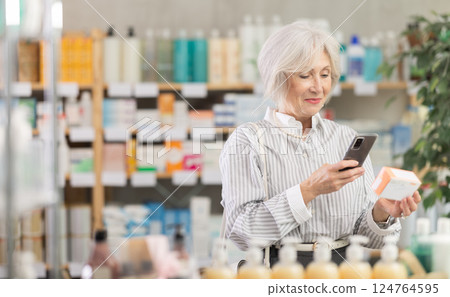 Elderly woman in summer clothes scans code on package of pills to check expiration date 124764595