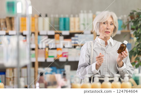 Elderly woman chooses syrup at pharmacy 124764604