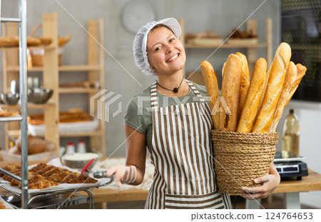 Bakery female seller stands proudly in front of fresh bread holding basket of freshly baked baguettes in kitchen 124764653