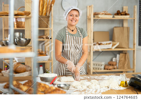 Female baker cutting raw dough with knife on kitchen table in private bakery Female baker cutting raw dough with knife on kitchen table in private bakery 124764685