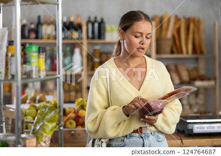 Customer in store is thinking about buying, considering packaging of dried meat delicacies 124764687
