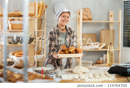 Positive female baker in uniform holding basket with croissants 124764700