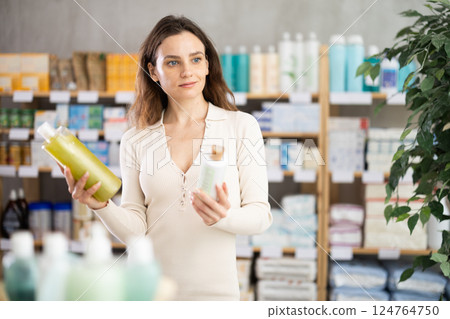 Female shopper in summer clothes chooses medicated shampoo at pharmacy 124764750