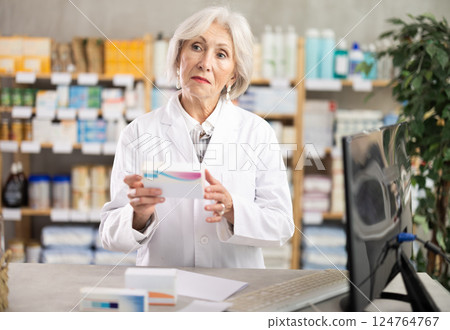 Mature female pharmacist offering a box of medicines 124764767