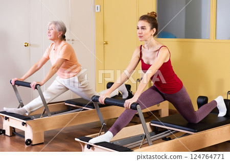 Elderly woman and young girl practicing on Pilates reformer 124764771