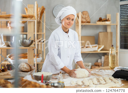 Young baker girl is standing near work table in kitchen, working with dough Young baker girl is standing near work table in kitchen, working with dough 124764778