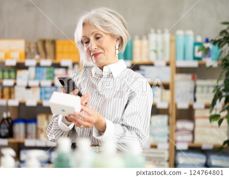 Elderly woman in summer clothes scans code on package of pills to check expiration date Elderly woman in summer clothes scans code on package of pills to check expiration date 124764801