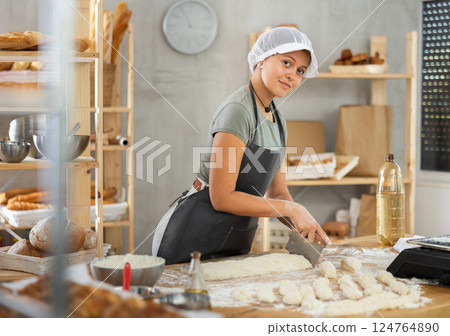 Female baker in uniform cutting raw dough with knife to make croissants or buns 124764890