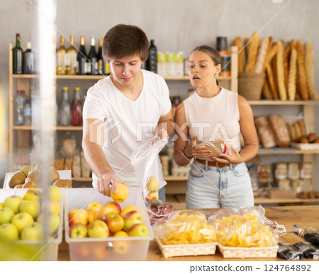 Young married couple buying ripe apples and other products in supermarket 124764892