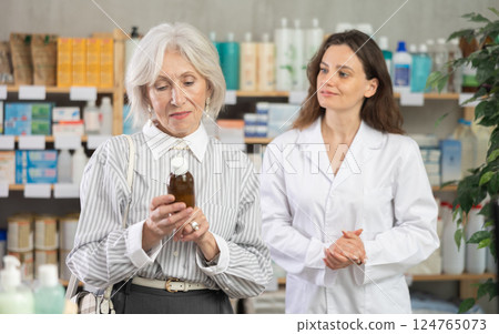 Mature woman choose antitussive syrup, woman pharmacist offers similar item 124765073
