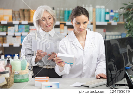 Female pharmacist with a package of pills working at a computer in front of a client Female pharmacist with a package of pills working at a computer in front of a client 124765079
