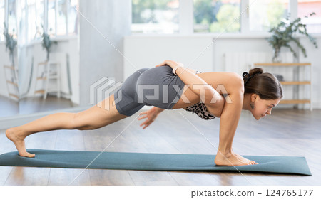 Yoga in sports gym. Girl performs side plank asana, vasishthasana Yoga in sports gym. Girl performs side plank asana, vasishthasana 124765177