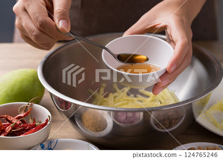 Spicy mango salad cooking, Hand adding fish sauce in bowl and mixing with ingredients Spicy mango salad cooking, Hand adding fish sauce in bowl and mixing with ingredients 124765246